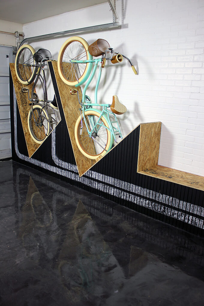 A unique way to store your bikes in the garage - a DIY wall-mounted bike rack with a bench. It takes up little space depth wise, you can store two bikes, it gives you a place to sit down AND the front is painted with chalkboard paint so the front design can always change.
